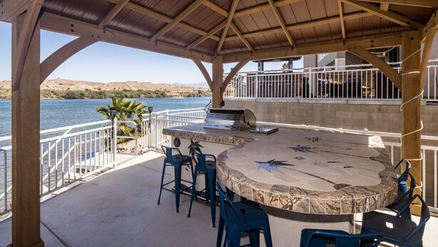 Une terrasse extérieure équipée d’un barbecue, d’un espace salon et offrant une vue sur un plan d’eau.