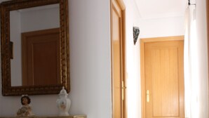 Un pasillo con una puerta de madera, un espejo y un aparador con objetos decorativos.