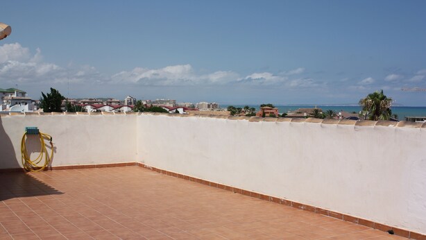 Una terraza en la azotea con vistas al mar y edificios a lo lejos.