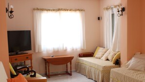 Una habitación con sofá, dos camas individuales, televisión, escritorio y ventana con cortinas.