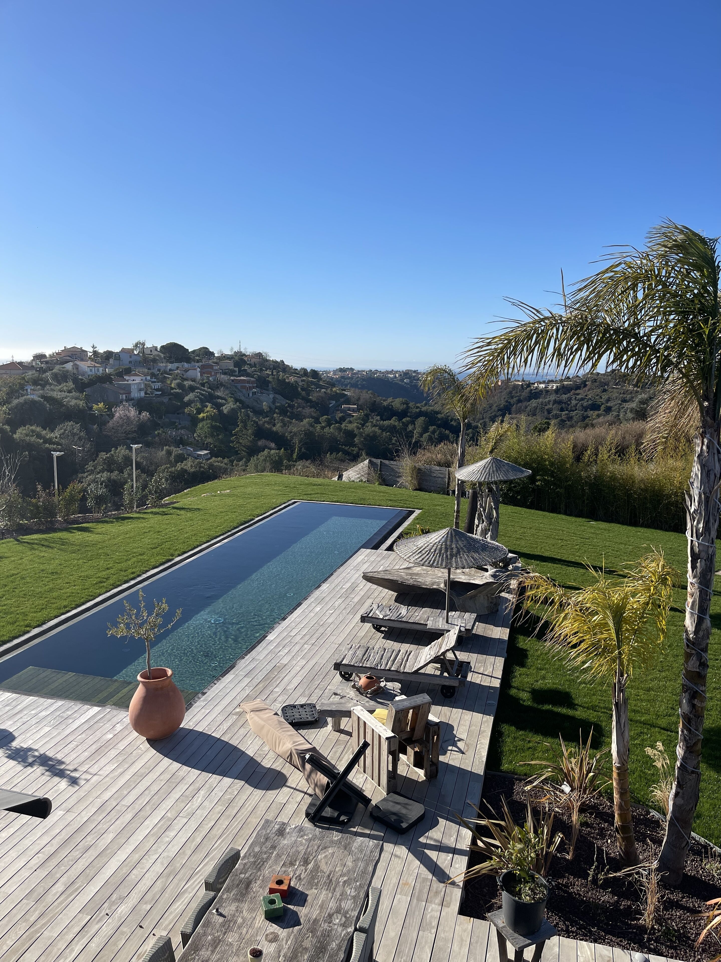 Una terraza de madera con piscina, sillas de descanso y vistas a un pueblo en la ladera.