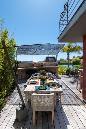 An outdoor dining area with a stone fireplace, wooden deck, and a view of a golf course. - Villa With Heated Pool Sea View (Nice)