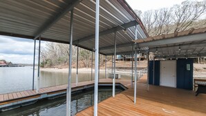 Eine überdachte Holzterrasse mit Blick auf ruhiges Wasser und entfernte Gebäude.