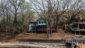 Ein zweistöckiges Haus mit blauer Fassade, umgeben von Bäumen und einem kleinen Teich.