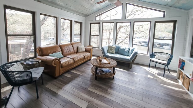 Ein geräumiges Zimmer mit Deckenventilator, großen Fenstern, einem braunen Ledersofa, einem blauen Sofa, einem Korbtisch und einem schwarzen Metallstuhl.