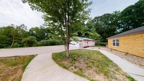 A wooden cabin with a stone foundation, a concrete driveway, and a well-maintained lawn.