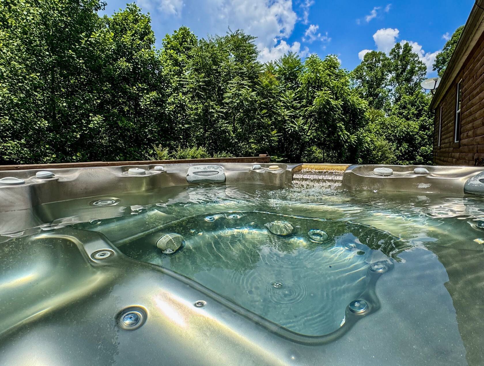 A hot tub with multiple seating areas, surrounded by lush greenery and a clear blue sky.