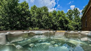 A hot tub with multiple seating areas, surrounded by lush greenery and a clear blue sky.