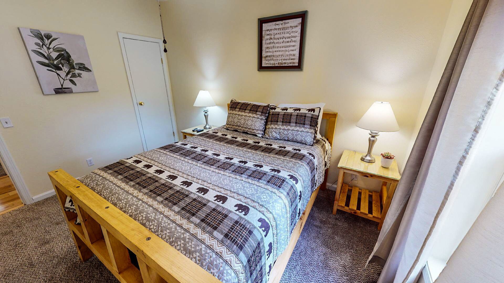A bedroom with a bed, two bedside tables, a nightstand, a bench, a wall-mounted lamp, and a framed picture.
