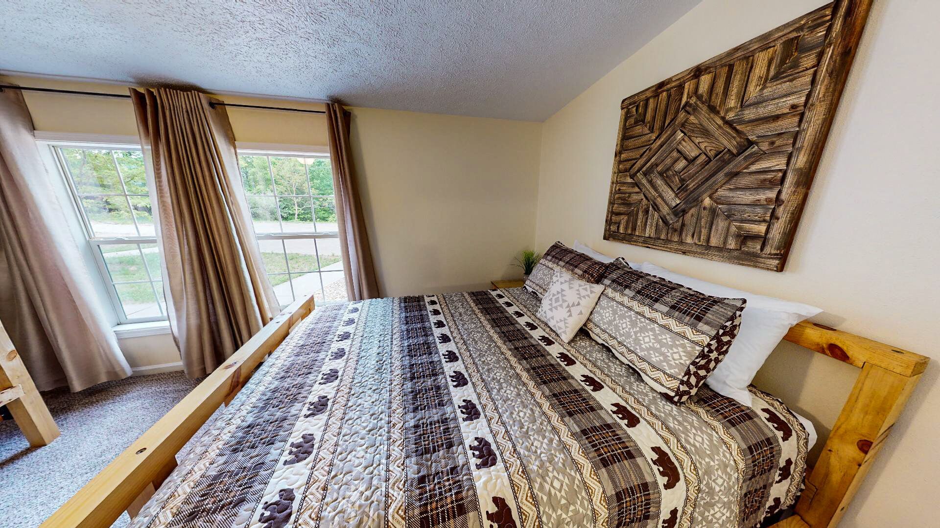 A bedroom with a bed, a wooden headboard, a window with curtains, and a wall-mounted wooden artwork.