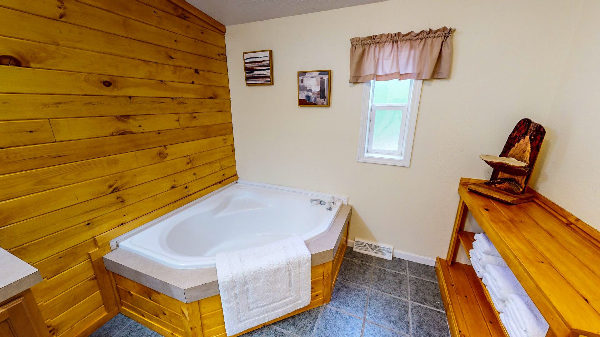 A wooden cabin bathroom with a wooden bathtub, a window with curtains, and a wooden bench with towels.