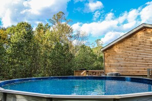 A swimming pool surrounded by a wooden cabin with a deck, set against a backdrop of trees and a clear sky. - Secluded Black Bear Lodge w/ Private Pool & Hot Tub near Hocking Hills Ohio (Nelsonville)