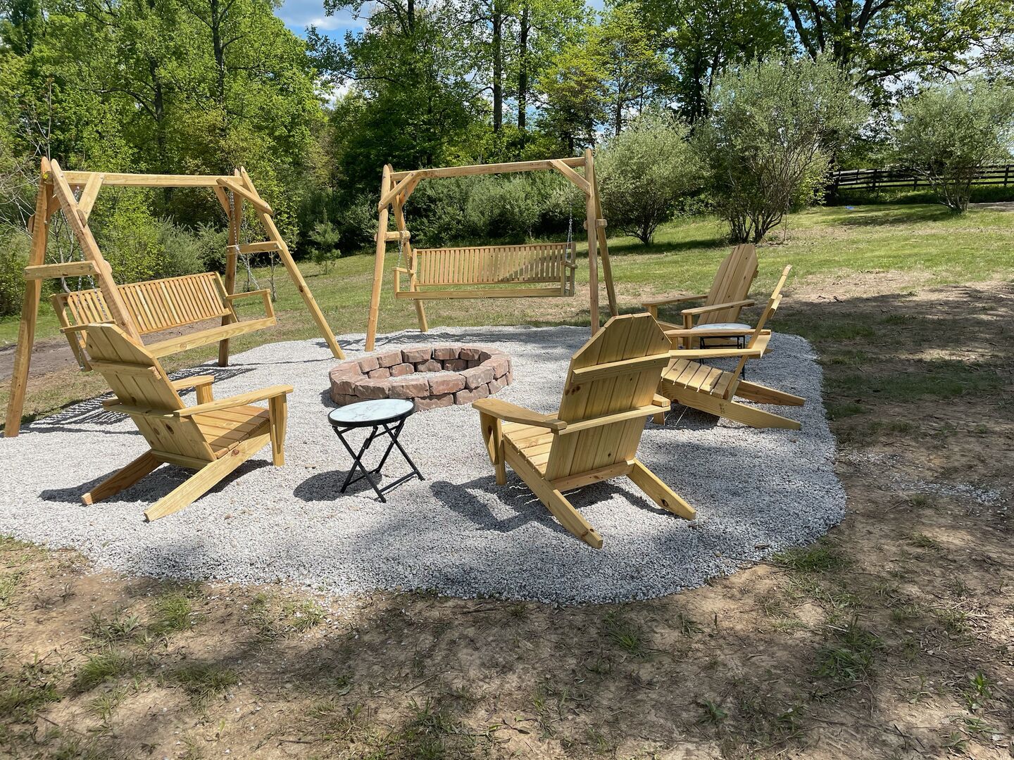 Een houten terras buiten met een vuurkorf en schommelsets.