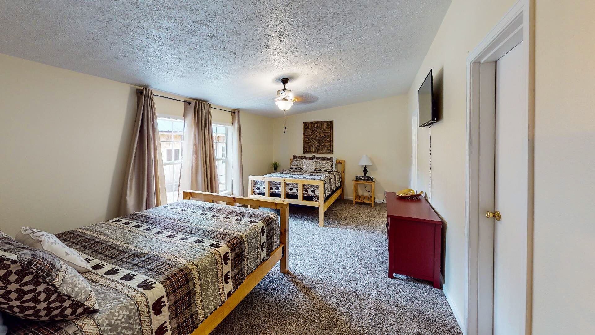 A bedroom with two beds, a ceiling fan, a TV, and a small table.