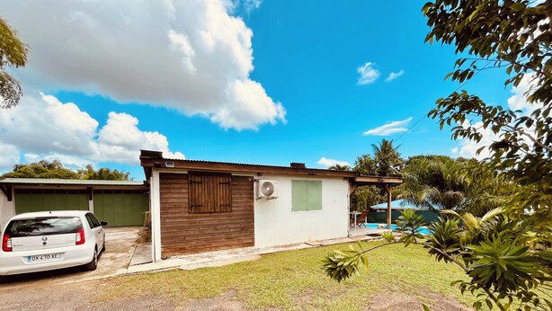 A small, single-story house with a white exterior and a brown wooden door. - Creole-style house with a pool and access to the river (Lamentin)