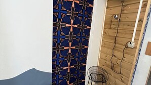 A room with a bed, a small table with a chair, a wall-mounted fan, and a patterned door. - Creole-style house with a pool and access to the river (Lamentin)