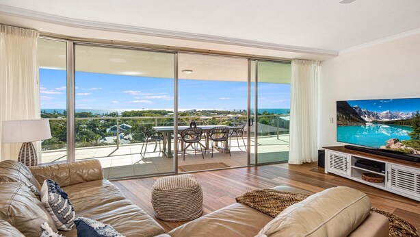 Uma sala de estar ampla, com uma televisão grande, assentos confortáveis e uma varanda com vista panorâmica.