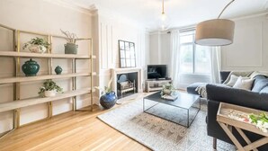 A modern living room with a fireplace, a sofa, a coffee table, and a TV. - Beautiful 5 Bedroom Home With Garden in South Kensington (London)
