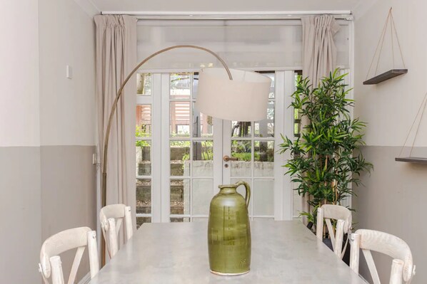 Enjoy meals in this dining area with a long table for four, a pitcher, and a view of lush greenery.