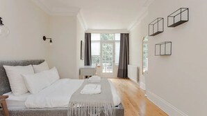 A modern bedroom with a bed, a desk, and a view through a window. - Beautiful 5 Bedroom Home With Garden in South Kensington (London)