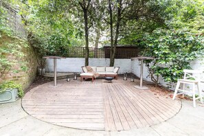 Relax in a tranquil outdoor space with a circular deck, sofa, and chairs, surrounded by a low wall and shaded by trees.