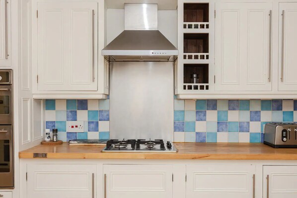 A kitchen with white cabinets, a stainless steel range hood, a gas stove, a toaster, and a tiled backsplash.