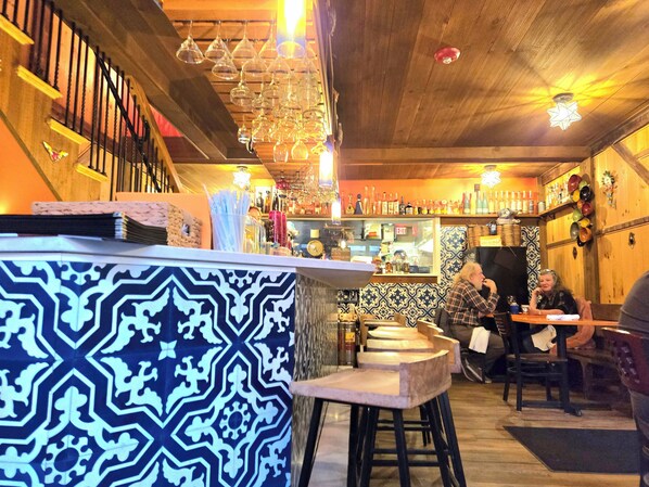 A bar area with a patterned counter, stools, and hanging wine glasses.