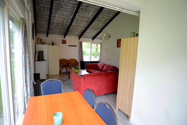 A compact living space with a dining area, a red sofa, and a kitchen area. - Vakantie Zuid Limburg (Simpelveld)