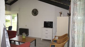 Una sala de estar con televisor, un mueble blanco, sillas de mimbre, un sofá rojo y un reloj en la pared.