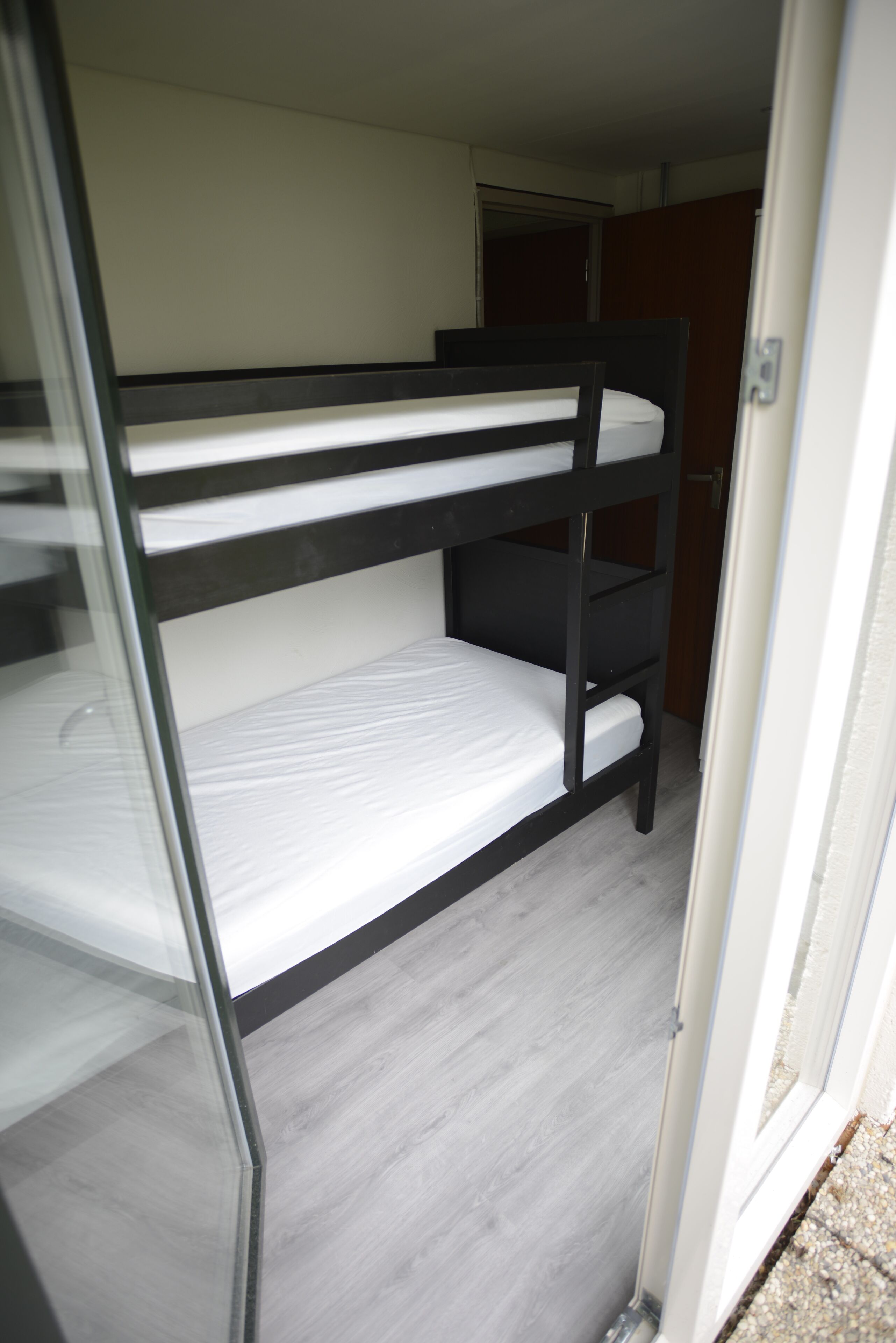 Un letto a castello in una stanza con una porta in vetro e un pavimento in legno.