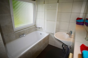 A bathroom with a bathtub, sink, and window. - Vakantie Zuid Limburg (Simpelveld)