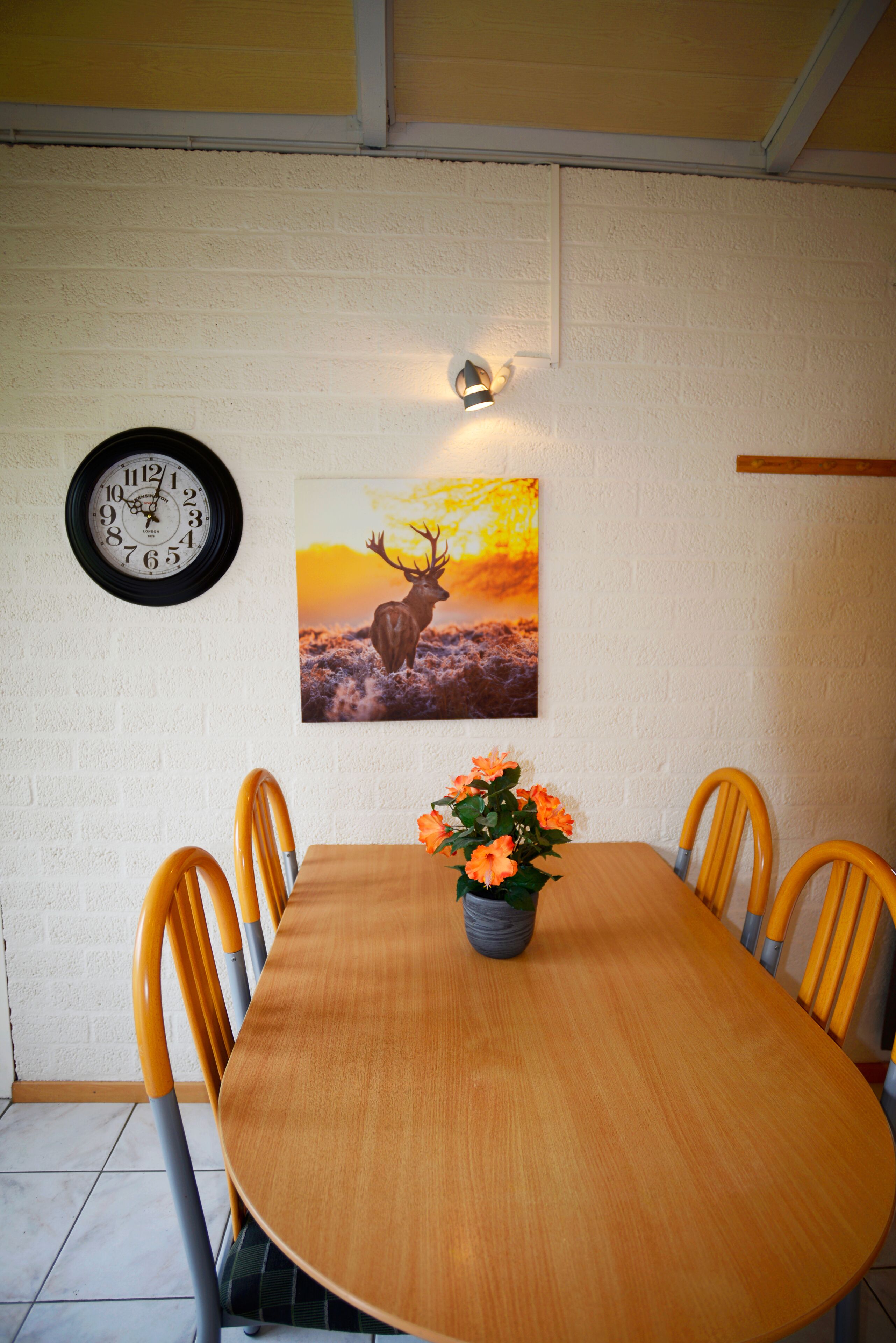 A dining table with four chairs, a clock, and a wall-mounted picture of a deer.