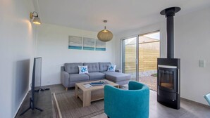 A modern living room with a grey sofa, teal armchair, and a wooden coffee table. A black wood-burning stove is visible on the right. - Tal Er Forn - PLOUHARNEL (PLOUHARNEL)