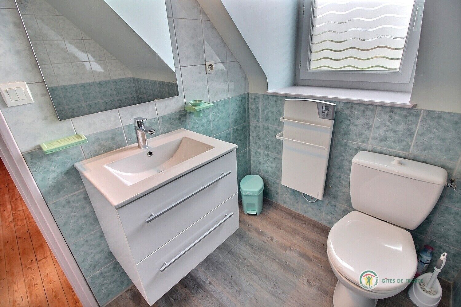 Een moderne badkamer met een wastafel, badkamermeubel, toilet en een raam met een golfpatroon.