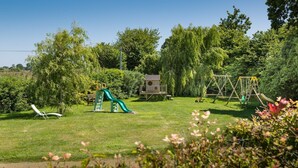 A playground with a slide and swings in a grassy area surrounded by trees. - L'Hortensia - PLEUDANIEL (PLEUDANIEL)