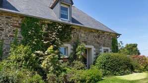 A stone house with a steeply pitched roof, a small dormer window, and a garden with various plants and shrubs. - L'Hortensia - PLEUDANIEL (PLEUDANIEL)