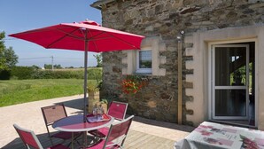 A stone building with a patio table and chairs, a red umbrella, and a window with a flower box. - L'Hortensia - PLEUDANIEL (PLEUDANIEL)