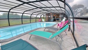 Une piscine couverte avec des chaises longues et vue sur l’extérieur.