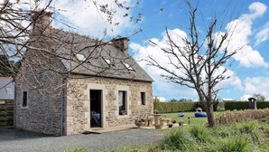 A stone cottage with a door open, a small window, and a garden with a bench and potted plants. - Amzerzo - PLOUBAZLANEC (PLOUBAZLANEC)
