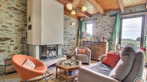 A cozy living room with a stone wall, a fireplace, a sofa, a rocking chair, and a wooden cabinet. - Amzerzo - PLOUBAZLANEC (PLOUBAZLANEC)
