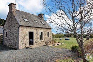 Une maison en pierre avec un toit en pente, un petit porche agrémenté de plantes en pot et un ciel dégagé.