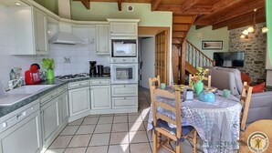 A kitchen with white cabinets, a microwave, and a stove. There is a dining table with chairs and a TV in the background. - Amzerzo - PLOUBAZLANEC (PLOUBAZLANEC)