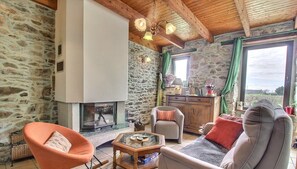 Una sala de estar acogedora con una pared de piedra, una chimenea, un sofá, un sillón mecedor y un aparador de madera.