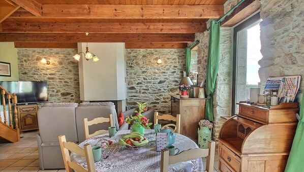 Una habitación acogedora con pared de piedra, muebles de madera, una mesa de comedor con mantel estampado y un televisor sobre un mueble.
