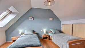 Une chambre avec deux lits en bois, une lucarne et un plafond en pente.