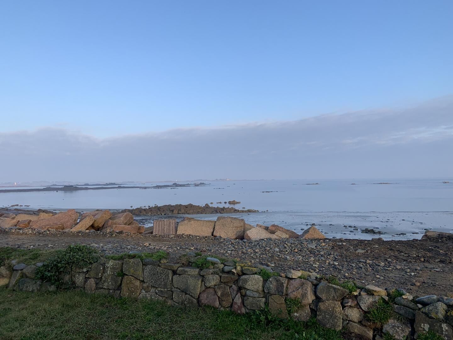 A coastal landscape with a stone wall and rocky shore.