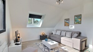 Ein modernes Wohnzimmer mit Sofa, Couchtisch, Beistelltisch, Lampe und einem kleinen Teppich. Ein Fenster bietet Blick ins Grüne.