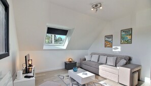 A modern living room with a sofa, a coffee table, a side table, a lamp, and a small rug. There is a window with a view of greenery outside.