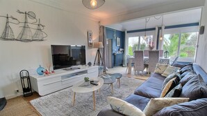 A modern living room with a large flat-screen TV, a sofa, a coffee table, and a dining area with a table and chairs. - Villa Sérénité - PERROS GUIREC (PERROS GUIREC)