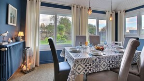 A dining area with a table set for four, large windows, and a view of greenery outside. - Villa Sérénité - PERROS GUIREC (PERROS GUIREC)